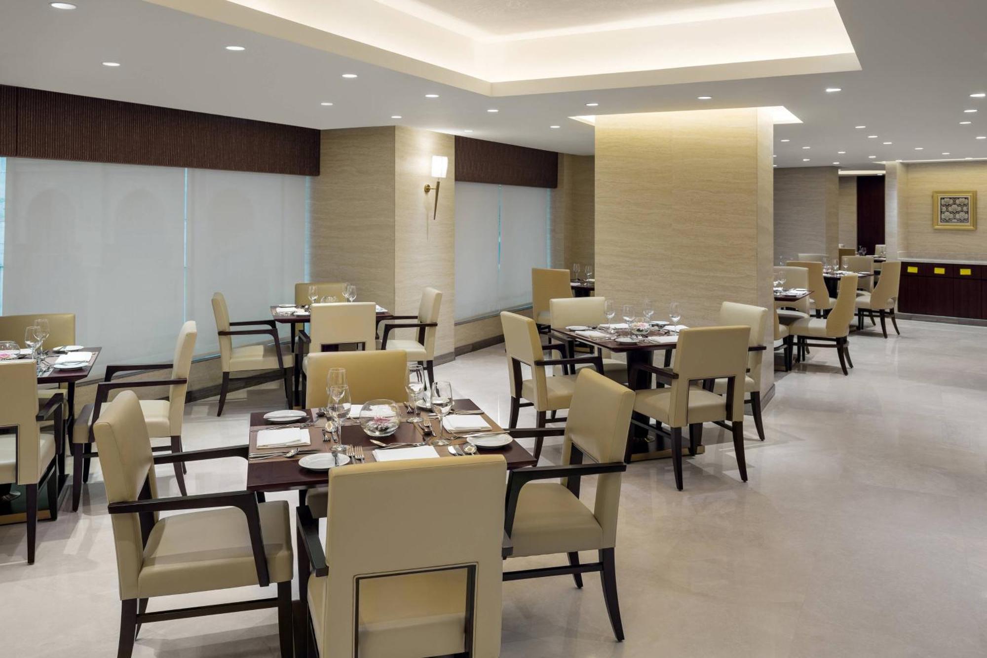 Sheraton Makkah Jabal Al Kaaba Hotel Mecca Екстер'єр фото The photo shows a modern restaurant interior. It features several dining tables, each set with utensils and tableware. The chairs are upholstered in a light fabric, and the overall decor is sleek and minimalistic, with soft lighting from overhead fix