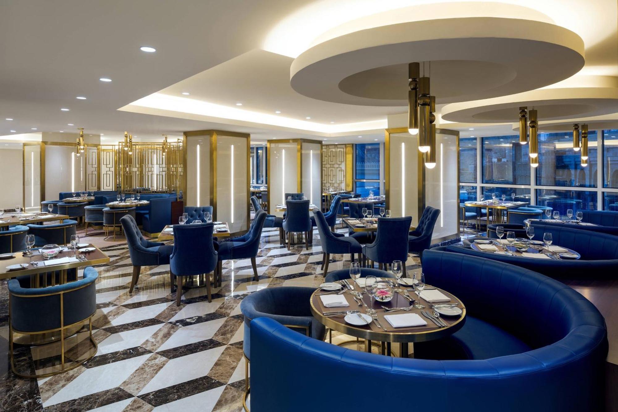 Sheraton Makkah Jabal Al Kaaba Hotel Mecca Екстер'єр фото The photo shows the interior of a modern restaurant. The design features elegant curved blue seating arranged around round tables with plates and glassware set for dining. The flooring is a striking marble pattern, adding to the upscale ambiance. The